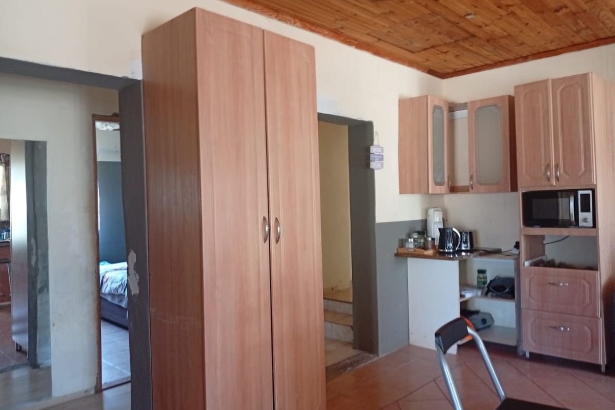 A kitchen area featuring timber ceiling panels, tiled flooring, and built-in cabinetry with integrated microwave housing, showing signs of wear and dated finishes.