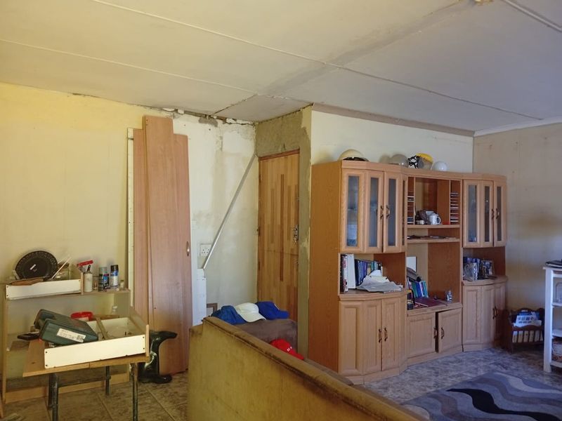 Living room area featuring built-in cabinetry and tiled flooring, currently showing significant signs of wear and unfinished wall and ceiling surfaces.