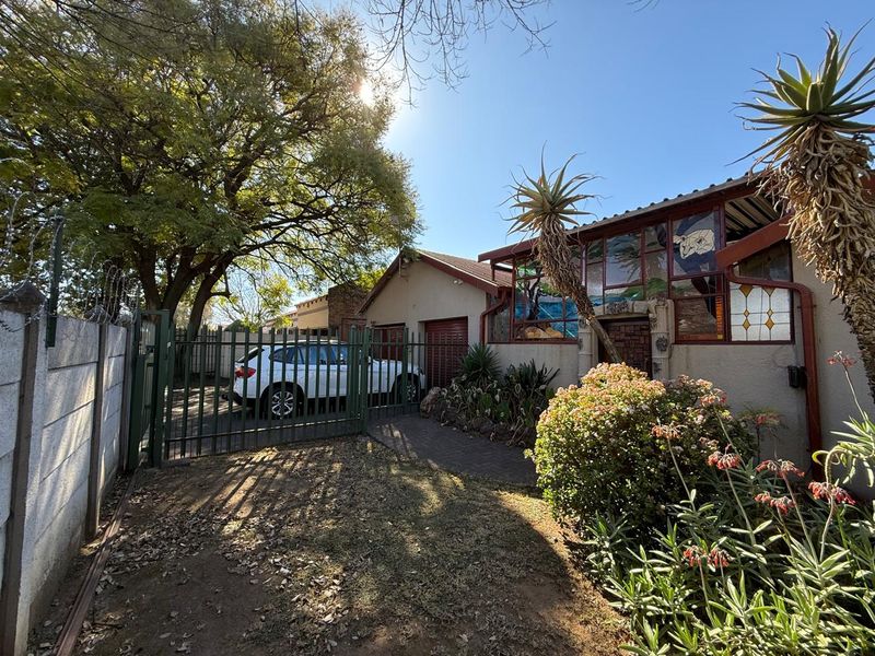 Front exterior view of the property featuring a paved driveway, metal security gate, boundary wall with razor wire, and decorative stained glass window detailing.