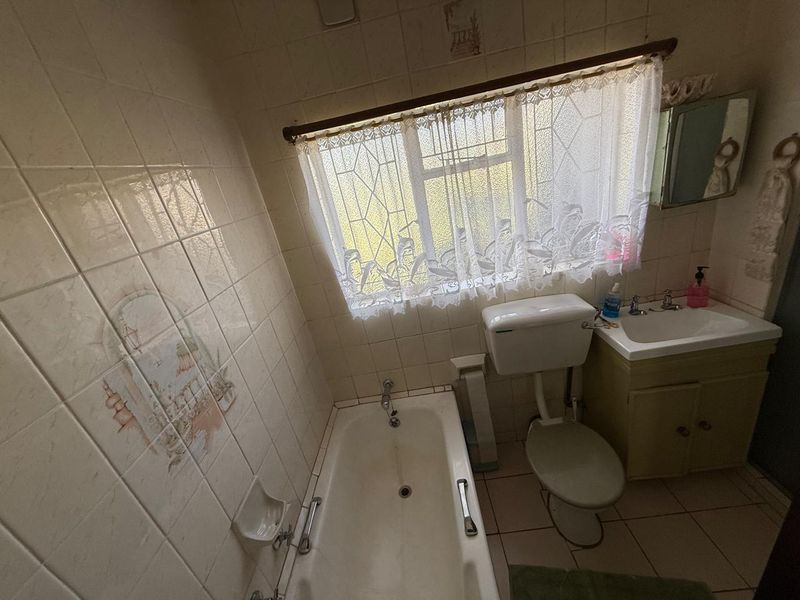 A dated bathroom featuring a built-in bathtub, vanity basin, and toilet, with original ceramic wall and floor tiling throughout.