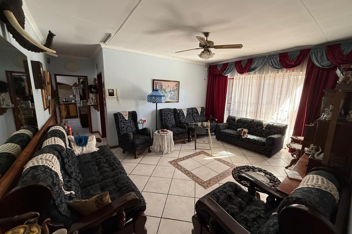 Spacious living room featuring ceramic floor tiles with a decorative inlay and a central ceiling fan, offering a traditional layout.