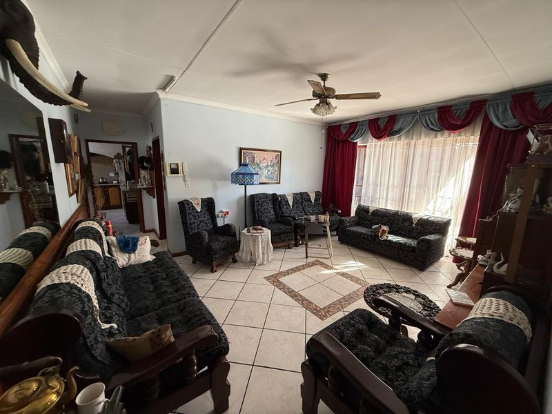 Spacious living room featuring ceramic floor tiles with a decorative inlay and a central ceiling fan, offering a traditional layout.