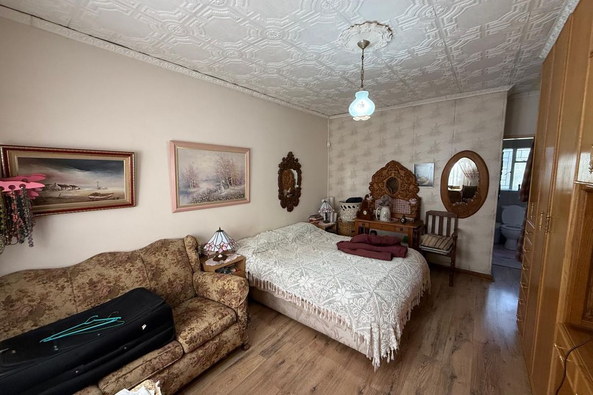 A bedroom featuring a decorative pressed metal ceiling, laminate flooring, and a built-in wardrobe, with an adjoining en-suite bathroom visible.