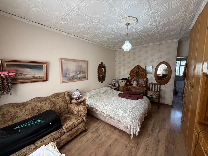 A bedroom featuring a decorative pressed metal ceiling, laminate flooring, and a built-in wardrobe, with an adjoining en-suite bathroom visible.