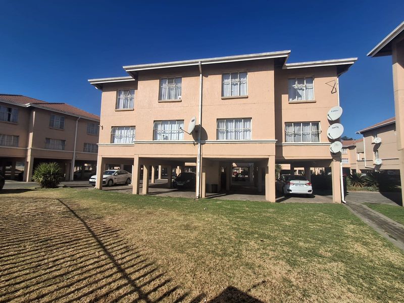 Exterior view of a multi-story apartment block featuring stilted ground-level parking, tiled roofing, and established lawn area.