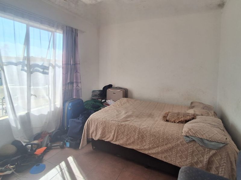 A bedroom featuring tiled flooring and a large window, currently showing signs of wear on the walls and ceiling.