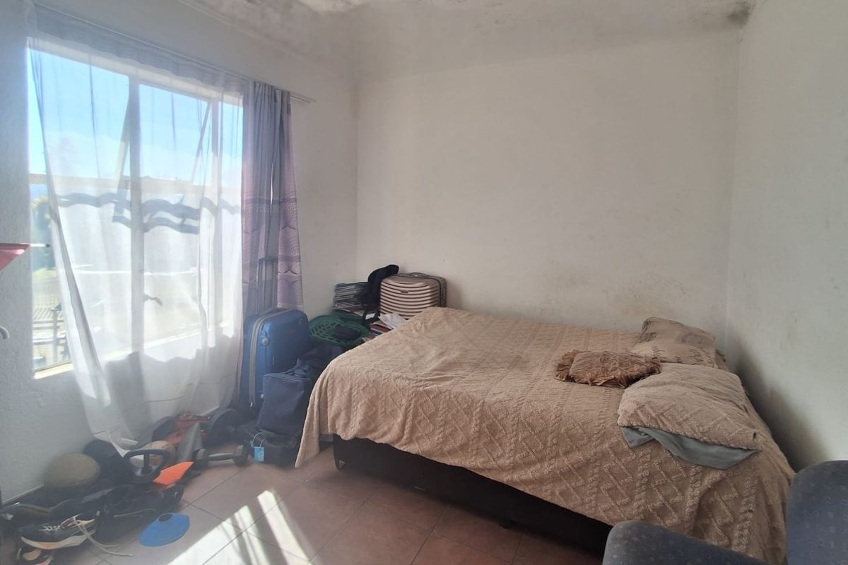 A bedroom featuring tiled flooring and a large window, currently showing signs of wear on the walls and ceiling.