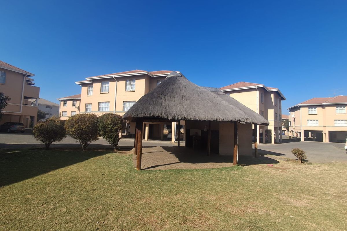 Communal outdoor area featuring a traditional thatched lapa, paved flooring, and landscaped lawn situated within a residential flat complex.