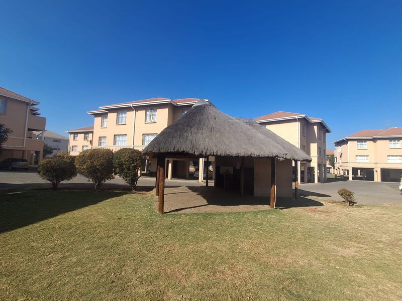 Communal outdoor area featuring a traditional thatched lapa, paved flooring, and landscaped lawn situated within a residential flat complex.