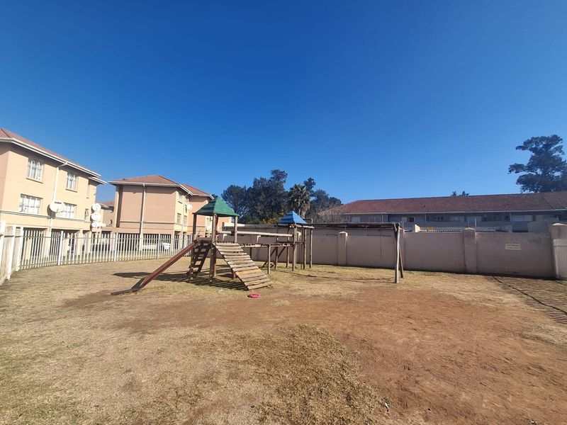 Communal garden area featuring a playground set, enclosed by perimeter walls and metal fencing within a residential flat complex.