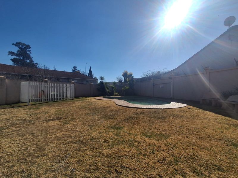 A private backyard area featuring a swimming pool with paved surround and high perimeter walls.