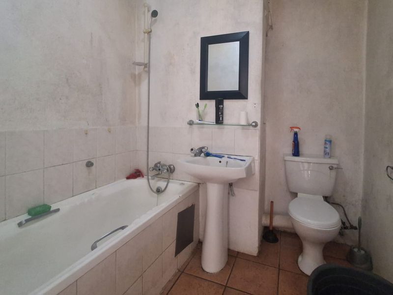 A dated bathroom featuring a standard bathtub, pedestal basin, and toilet, requiring significant cosmetic renovation and wall surface repairs.