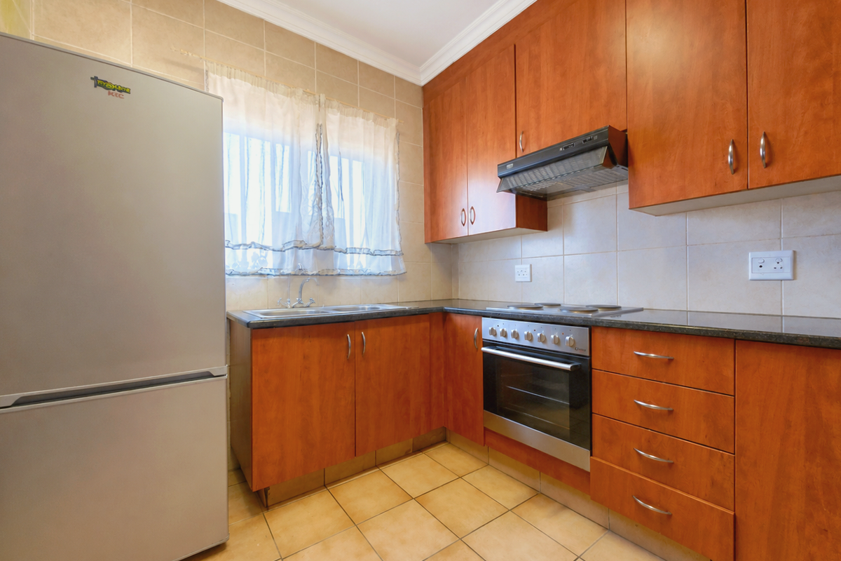 A functional kitchen featuring wood-finish cabinetry, granite countertops, a built-in oven with hob, and tiled flooring with a neutral backsplash.