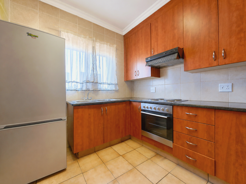 A functional kitchen featuring wood-finish cabinetry, granite countertops, a built-in oven with hob, and tiled flooring with a neutral backsplash.