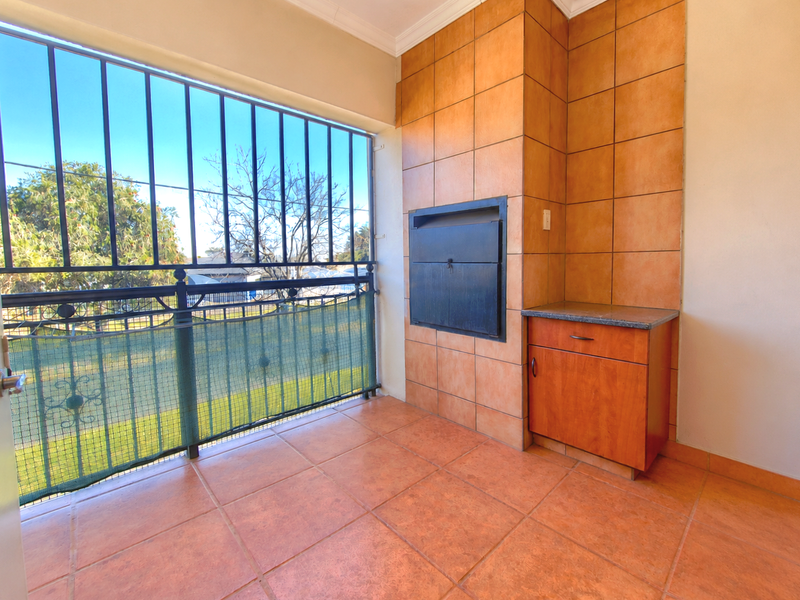 Covered balcony featuring a built-in braai, tiled flooring, and secure metal railings, offering a functional outdoor entertainment space.