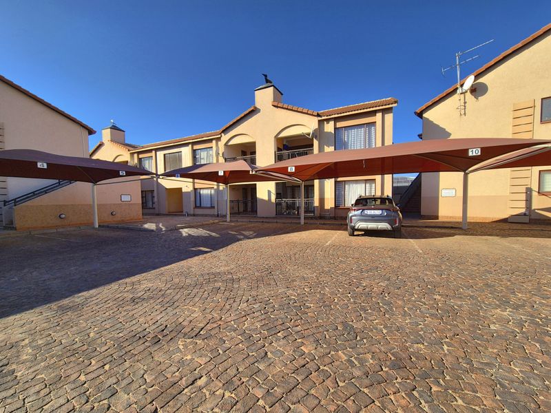 Exterior view of an apartment complex featuring a paved cobblestone driveway and multiple covered parking bays with shade cloth structures.