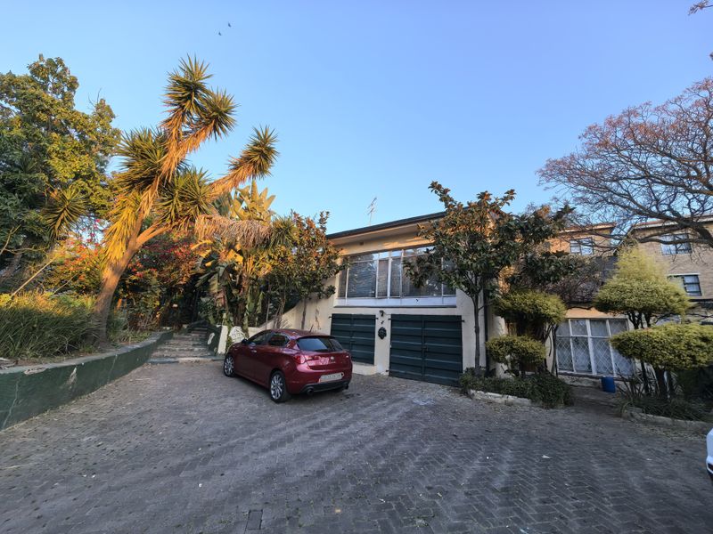 Front elevation of a two-story house featuring a paved driveway, double garage, and established garden with stone stairs leading to the entrance.