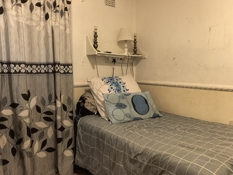 A compact bedroom featuring a wall-mounted shelf and decorative dado rail, currently requiring cosmetic updates to the wall finishes.