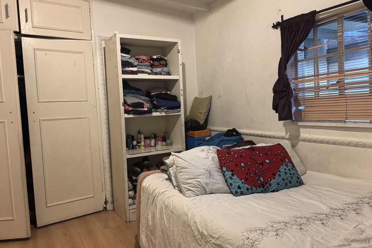 A bedroom featuring laminate flooring, built-in wardrobe storage, and decorative wall molding, requiring cosmetic updates to improve the overall finish.