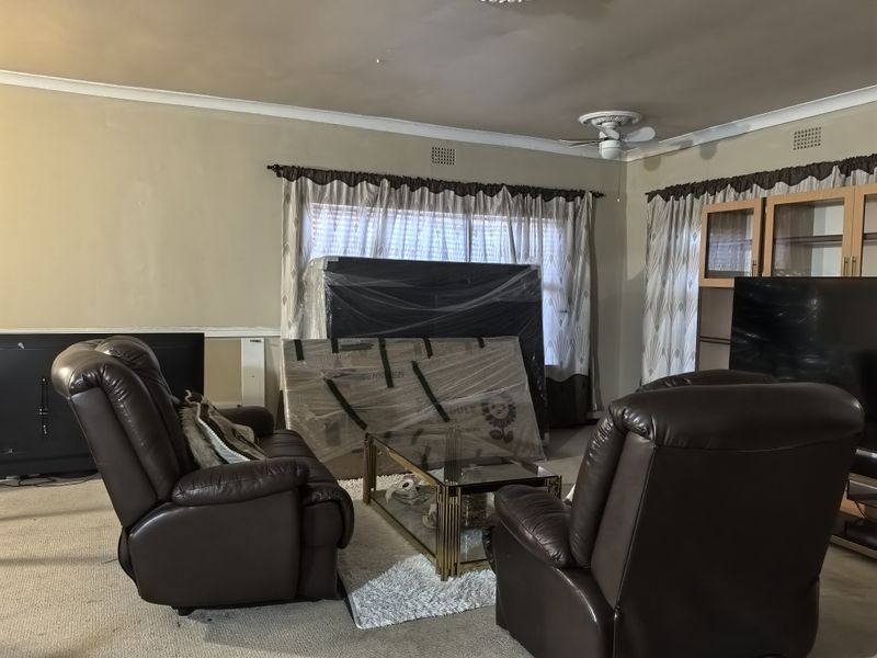 A living room featuring a ceiling fan, built-in cabinetry, and carpet flooring. The space shows signs of wear and requires cosmetic updates.