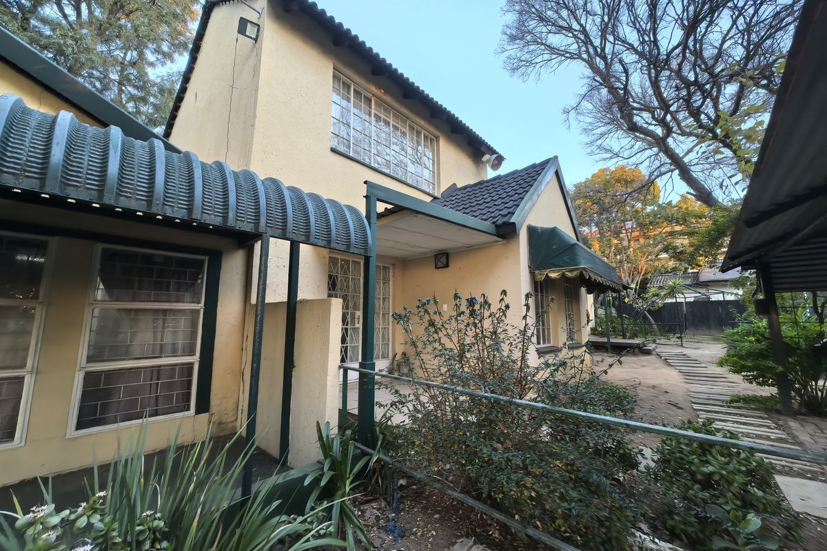 Rear view of a two-story house featuring a stucco facade, corrugated metal awning, and steel-framed windows with security bars.