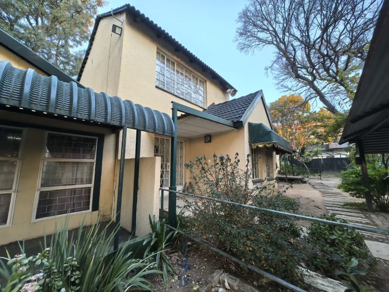 Rear view of a two-story house featuring a stucco facade, corrugated metal awning, and steel-framed windows with security bars.