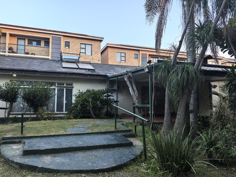 Rear view of the property featuring a covered patio area, concrete steps, and a solar water heating system installed on the roof.