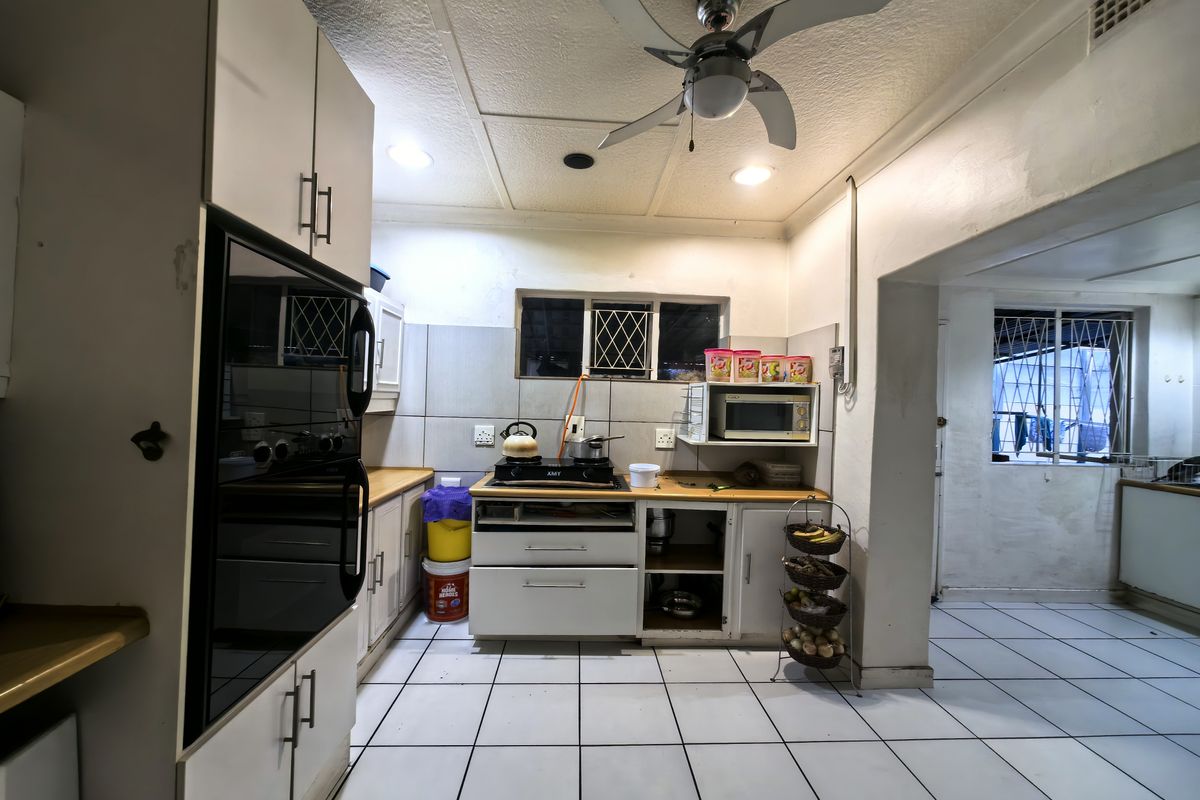 A functional kitchen featuring built-in cabinetry, a hob, and an integrated oven, with tiled flooring and security bars on the windows.
