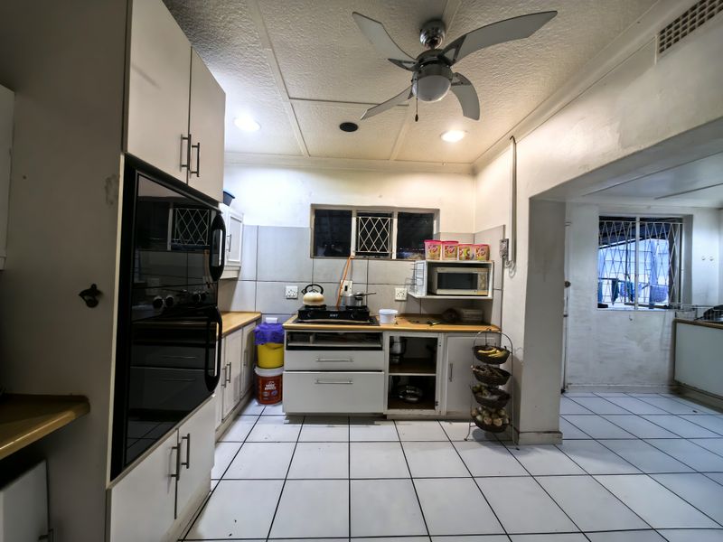 A functional kitchen featuring built-in cabinetry, a hob, and an integrated oven, with tiled flooring and security bars on the windows.