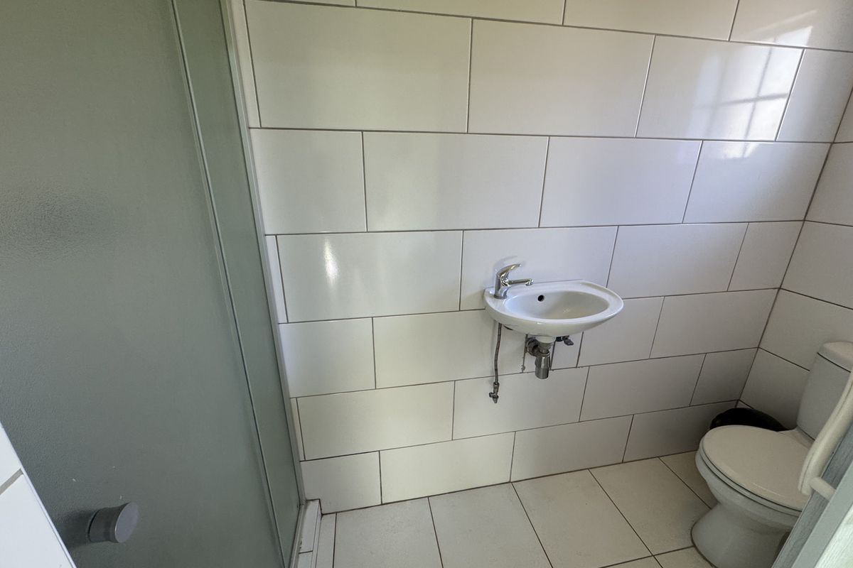 A clean, minimalist bathroom featuring a wall-mounted basin, toilet, and a glass-enclosed shower with modern white subway-style wall tiling.