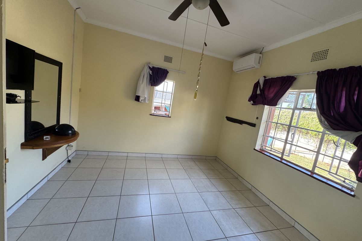 A vacant bedroom featuring tiled flooring, a ceiling fan, air conditioning, and security bars on the windows.