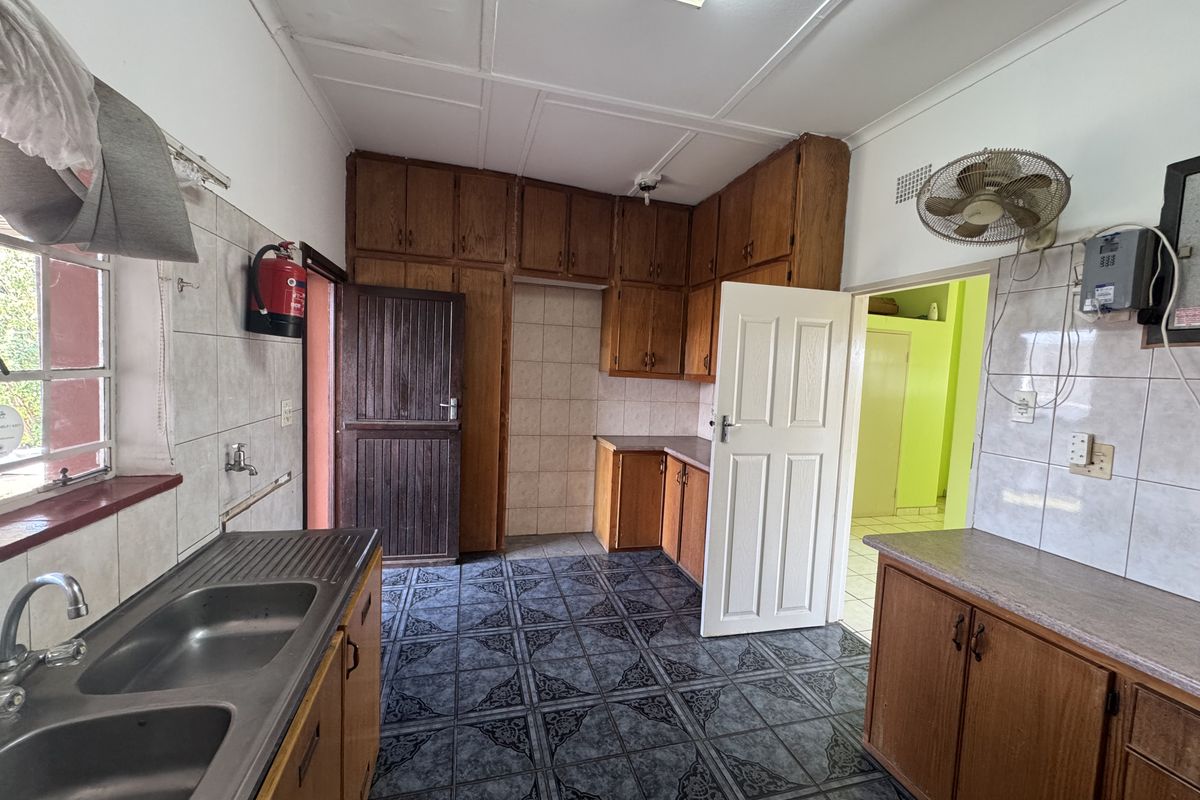 A dated kitchen featuring built-in wooden cabinetry, double stainless steel sink, tiled splashbacks, and tiled flooring, offering potential for modernization.