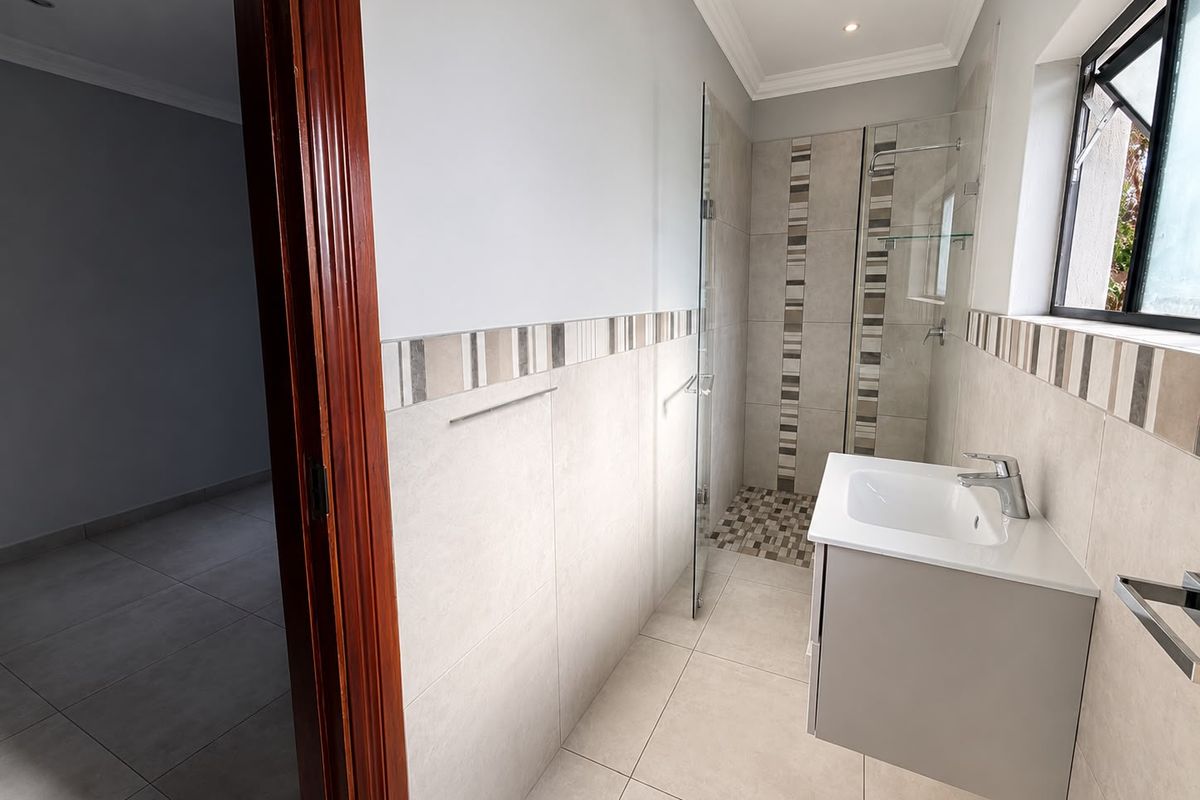 A modern, well-maintained bathroom featuring a wall-mounted vanity, glass-enclosed shower with decorative tile accents, and neutral floor-to-ceiling tiling.