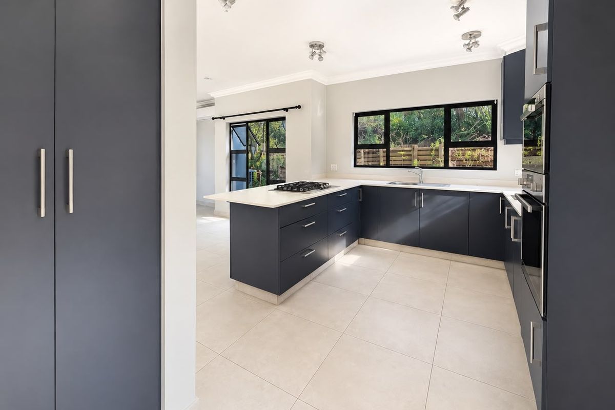 Modern kitchen featuring dark cabinetry, stone countertops, a gas hob, built-in oven, and large windows overlooking the garden.