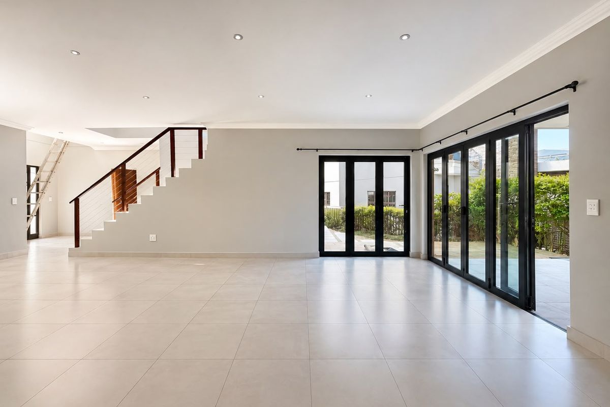 Spacious open-plan living area featuring neutral porcelain tiles, recessed lighting, and large black aluminium stacker doors providing seamless access to the outdoor area.