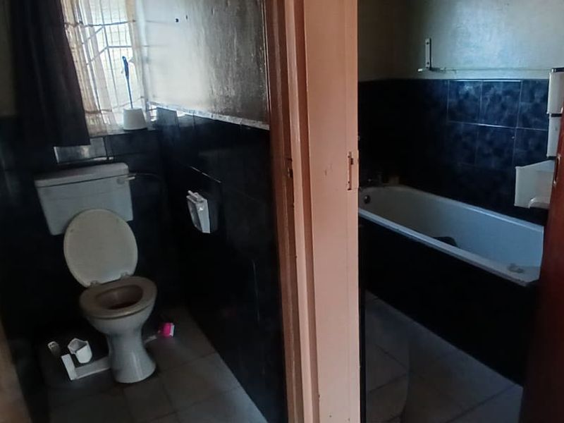 A dated bathroom featuring a standard toilet and a bathtub with dark wall tiling, requiring cosmetic updates to improve its overall condition.
