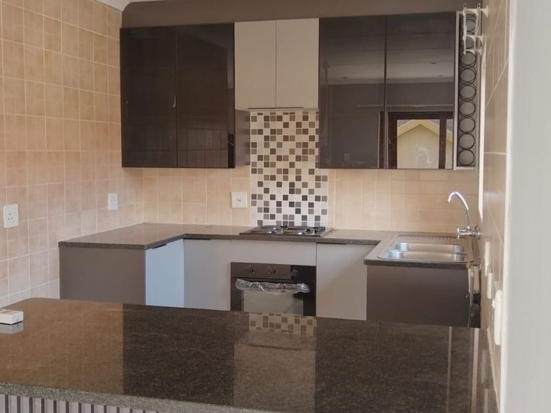 A modern kitchen featuring dark cabinetry, granite countertops, a built-in oven, gas hob, and a functional breakfast bar area.