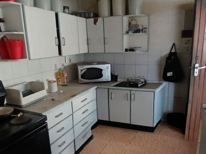 A dated kitchen featuring white cabinetry, tiled backsplash, and tiled flooring, offering significant potential for modernization and renovation.