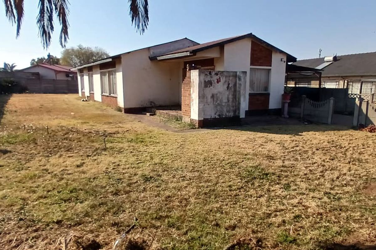 Rear view of a detached house featuring a large yard, brick and plaster facade, and precast concrete boundary walls.