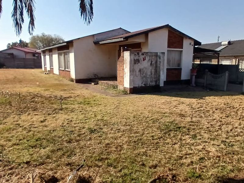 Rear view of a detached house featuring a large yard, brick and plaster facade, and precast concrete boundary walls.