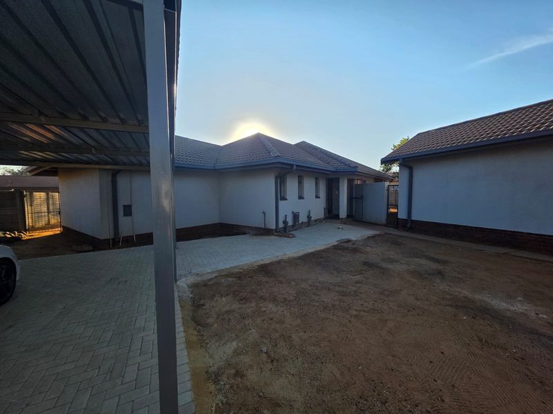 Rear exterior view of the house featuring a paved driveway, a metal carport structure, and an unlandscaped yard area.