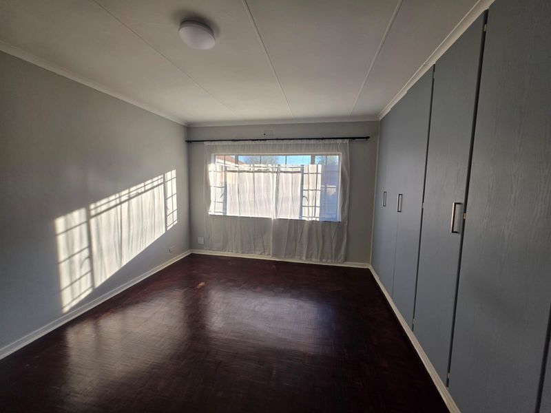 A bright, empty bedroom featuring dark parquet flooring and extensive built-in cupboard storage, offering a clean canvas for personalization.