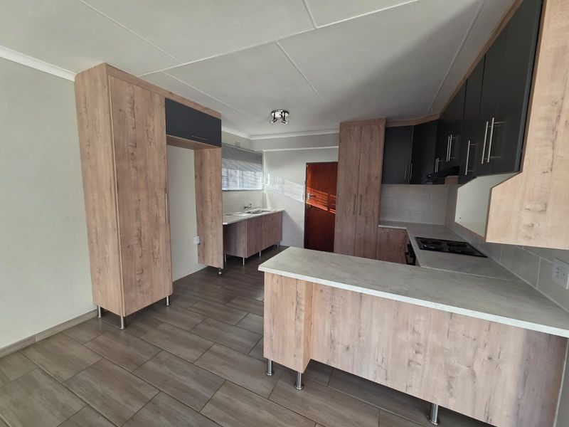 Modern kitchen featuring light wood-grain cabinetry, dark accent cupboards, integrated hob, and tiled flooring in an open-plan layout.