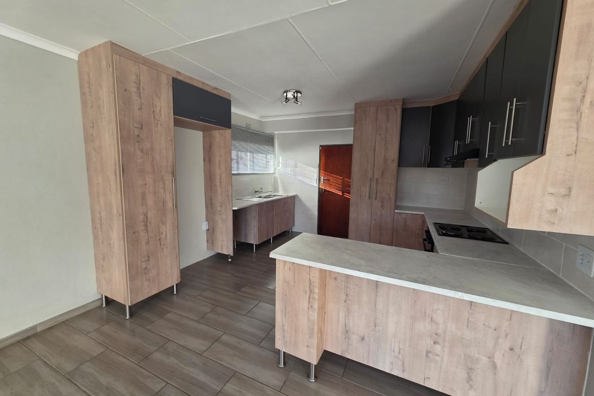 Modern kitchen featuring light wood-grain cabinetry, dark accent cupboards, integrated hob, and tiled flooring in an open-plan layout.