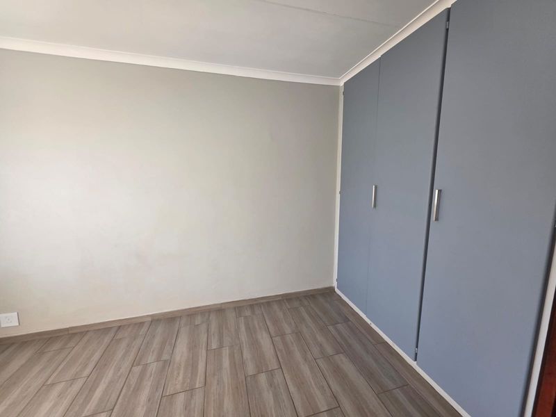 A clean, empty bedroom featuring modern laminate flooring and built-in cupboards with grey doors.