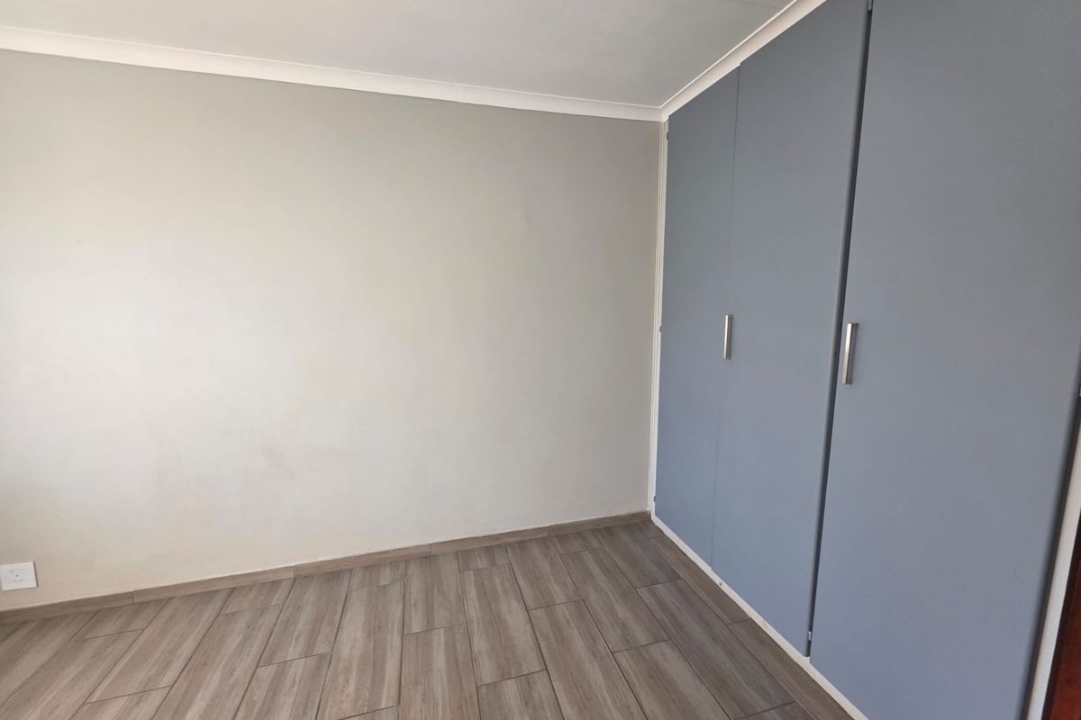 A clean, empty bedroom featuring modern laminate flooring and built-in cupboards with grey doors.