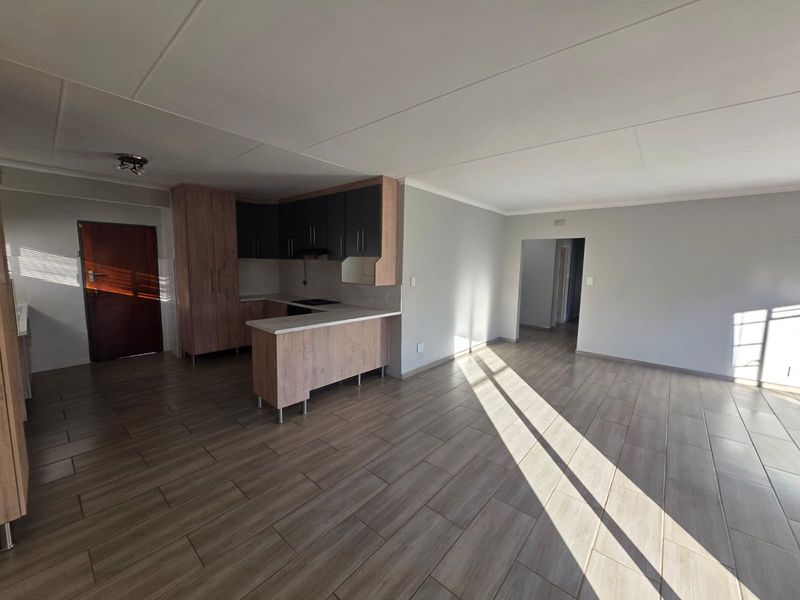 Spacious open-plan living area featuring modern wood-look laminate flooring and a functional kitchen with built-in cabinetry and a breakfast counter.