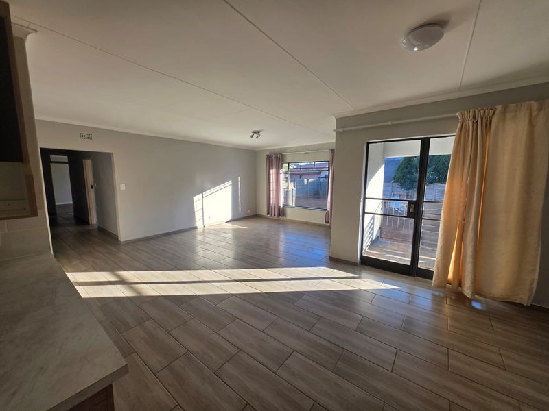 Spacious open-plan living area featuring modern tiled flooring, ample natural light, and direct access to an outdoor patio through a sliding glass door.