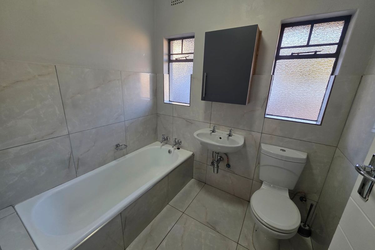 A functional bathroom featuring a bathtub, pedestal basin, and toilet with neutral wall and floor tiling and obscured glass windows.