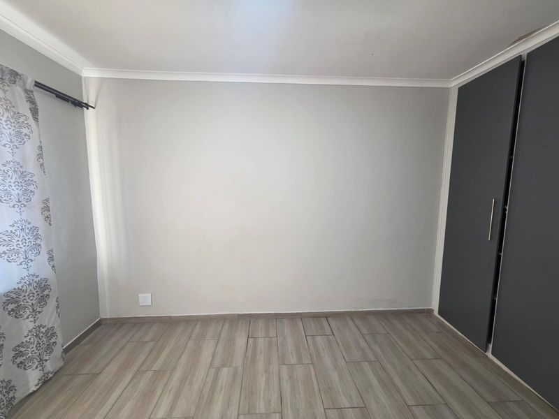 A clean, empty bedroom featuring modern wood-look tiled flooring and a built-in dark grey wardrobe.